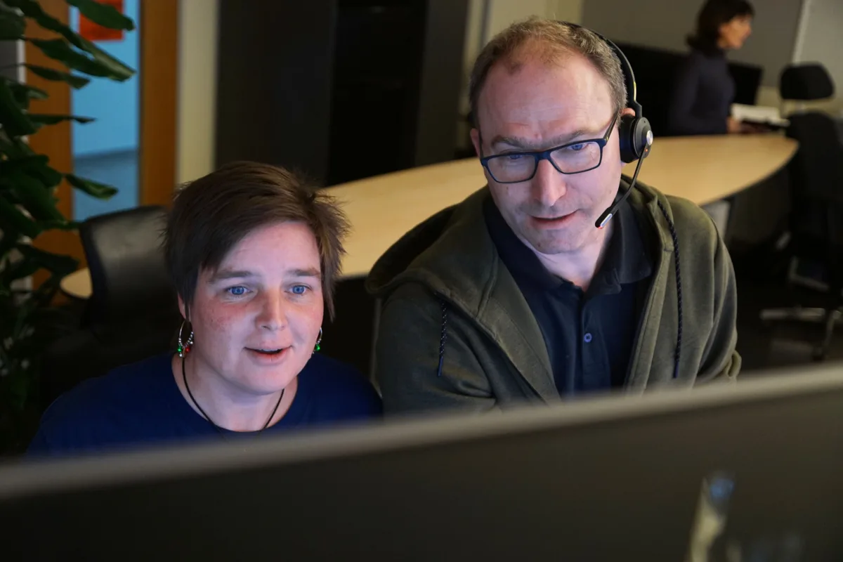 Man sieht eine Frau und einen Mann vor einem Bildschirm sprechen.